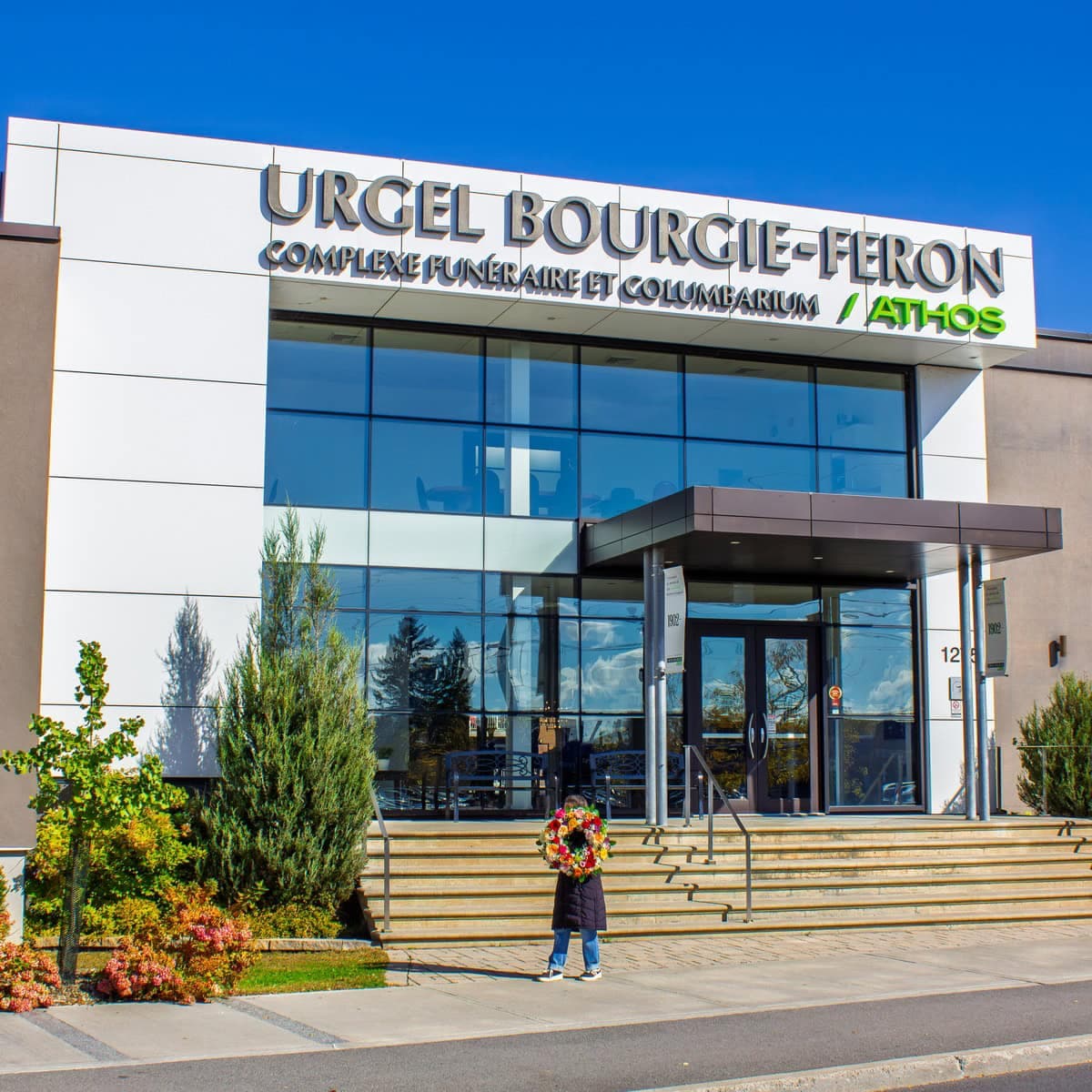 Person holding a colourful funeral wreath outside Urgel Bourgie in LaSalle