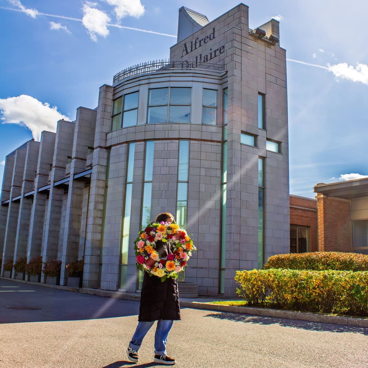 Person holding a colourful funeral wreath outside Yves Légaré on Newman Boulevard in LaSalle
