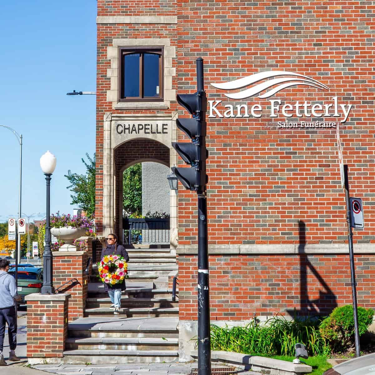 Person carrying a funeral wreath outside Kane & Fetterly in Côte-des-Neiges, Montreal