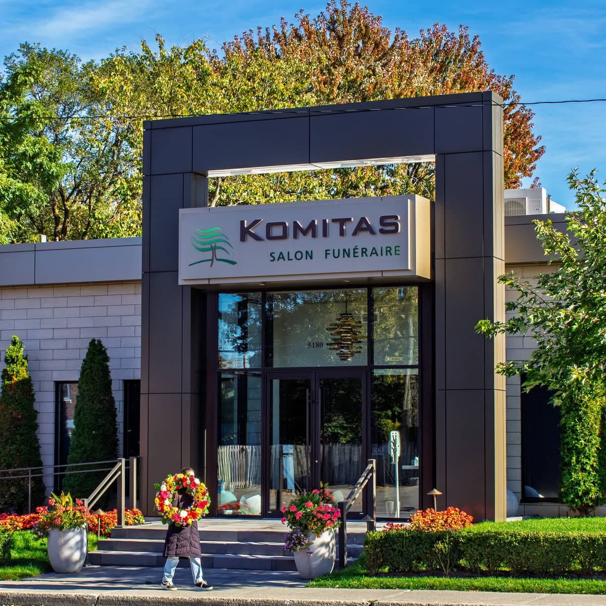 Person carrying a colourful funeral wreath outside Komitas Funeral Home in Ahuntsic-Cartierville