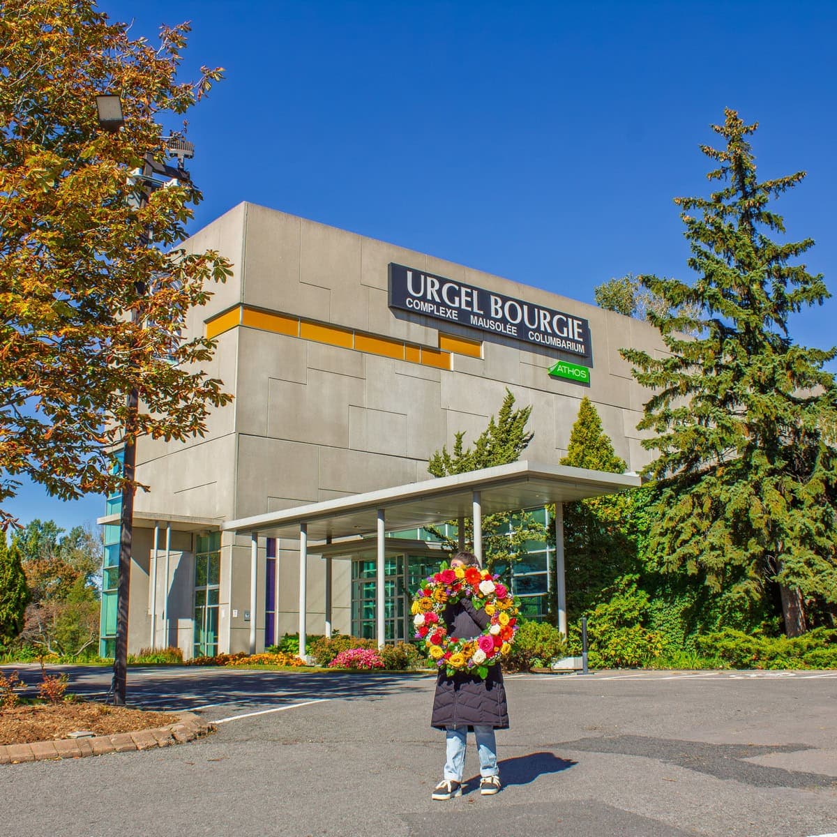 Person carrying a colourful funeral wreath outside Urgel Bourgie on Côte-de-Liesse in Saint-Laurent
